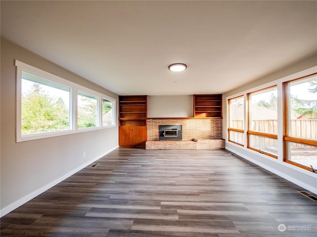 unfurnished living room with dark wood-type flooring, visible vents, built in features, baseboards, and a brick fireplace