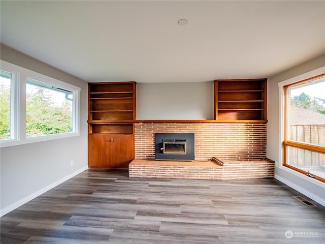 unfurnished living room with built in shelves, wood finished floors, visible vents, and baseboards