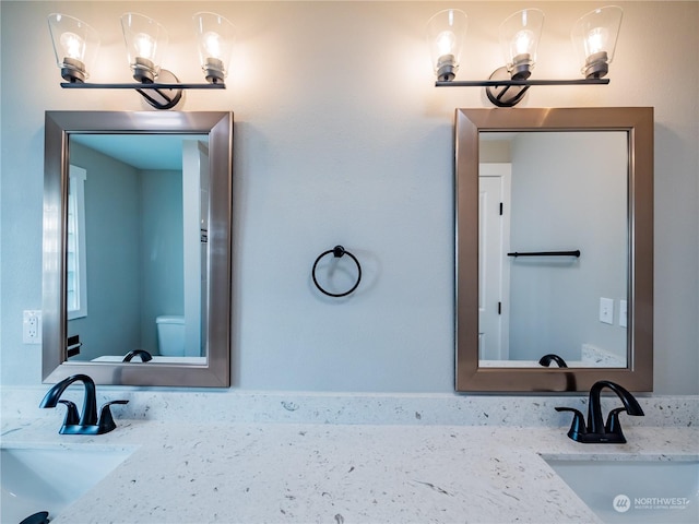 bathroom with a sink, toilet, and double vanity