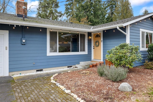 entrance to property with a shingled roof, crawl space, a chimney, and an attached garage