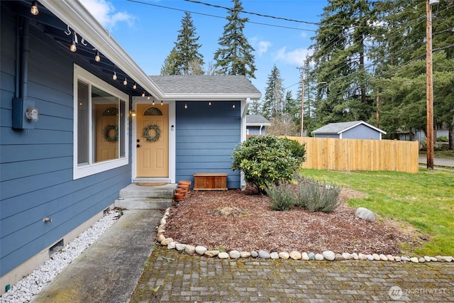 entrance to property featuring fence, a lawn, and roof with shingles