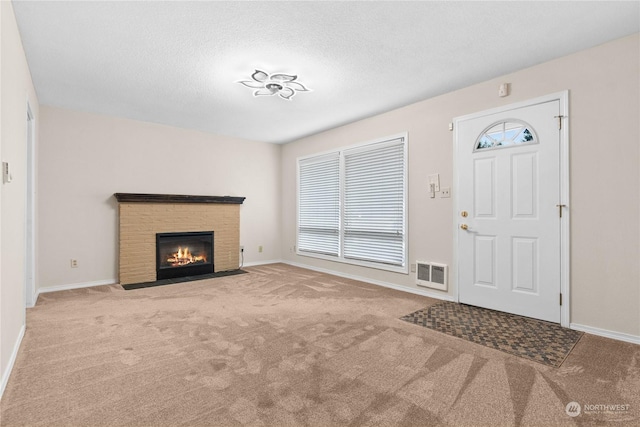 foyer entrance featuring a brick fireplace, a textured ceiling, and carpet