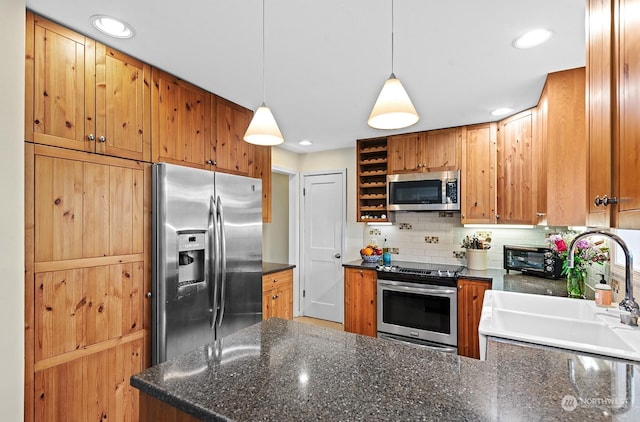 kitchen with sink, dark stone countertops, stainless steel appliances, decorative backsplash, and decorative light fixtures