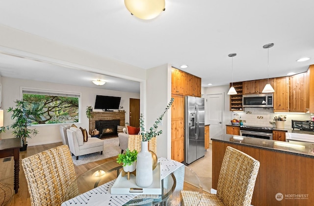 kitchen with tasteful backsplash, decorative light fixtures, appliances with stainless steel finishes, a fireplace, and light hardwood / wood-style floors