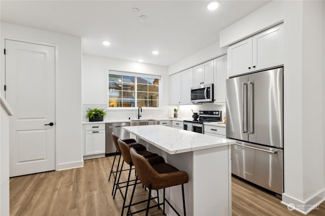 kitchen with a breakfast bar area, appliances with stainless steel finishes, a kitchen island, light stone countertops, and white cabinets