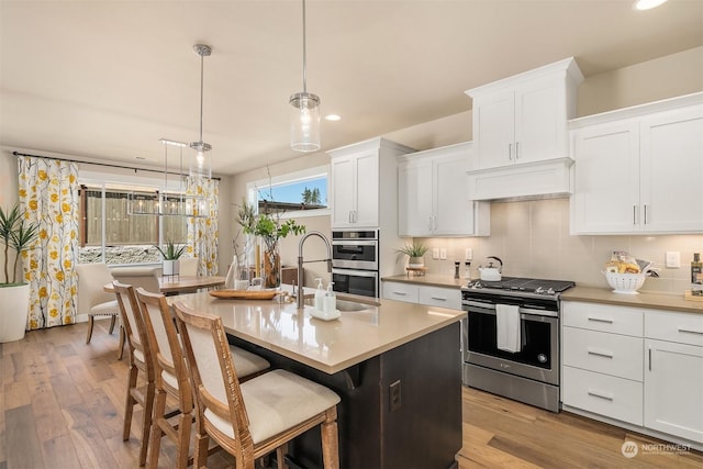 kitchen with white cabinetry, decorative light fixtures, stainless steel appliances, and an island with sink