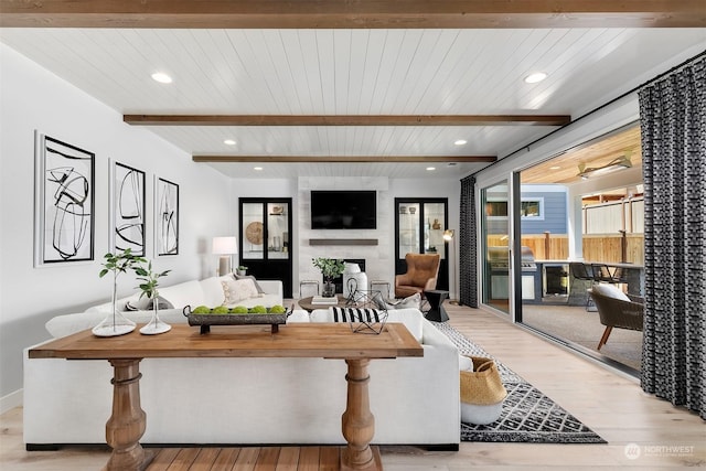 living room with a large fireplace, beam ceiling, and light wood-type flooring