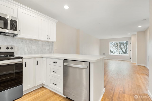 kitchen featuring white cabinetry, light hardwood / wood-style flooring, kitchen peninsula, stainless steel appliances, and decorative backsplash