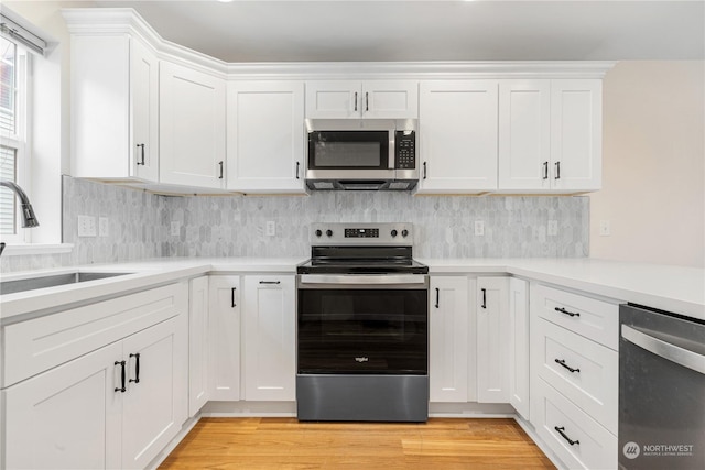 kitchen featuring sink, white cabinetry, stainless steel appliances, light hardwood / wood-style floors, and decorative backsplash