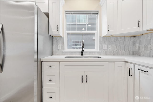 kitchen with tasteful backsplash, sink, white cabinets, and stainless steel refrigerator