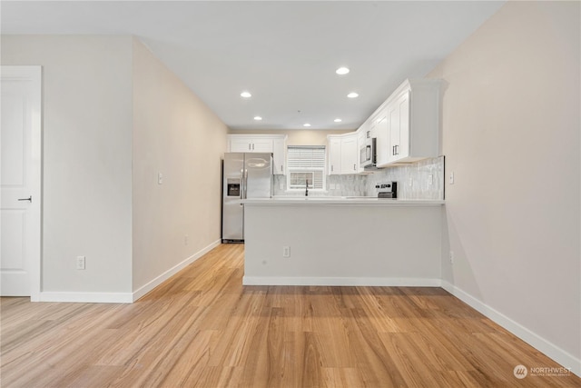 kitchen with appliances with stainless steel finishes, tasteful backsplash, white cabinets, kitchen peninsula, and light wood-type flooring