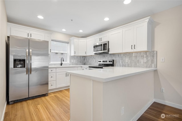 kitchen featuring sink, white cabinetry, light wood-type flooring, appliances with stainless steel finishes, and kitchen peninsula