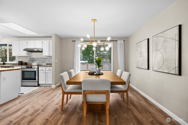 dining area with a healthy amount of sunlight, a chandelier, sink, and light wood-type flooring