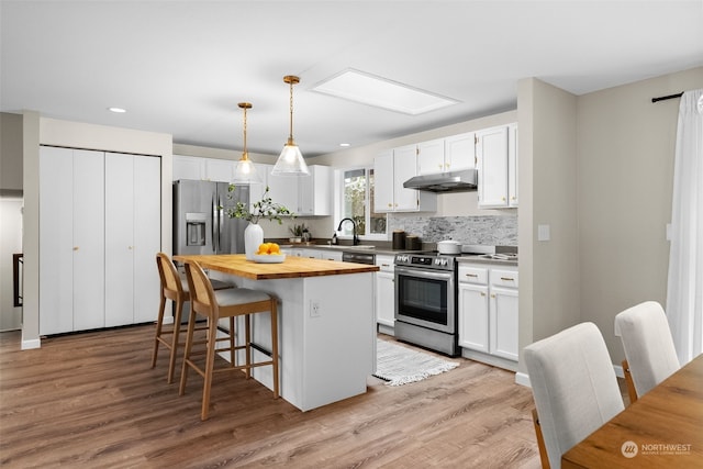 kitchen featuring white cabinetry, stainless steel appliances, a center island, a kitchen bar, and decorative light fixtures