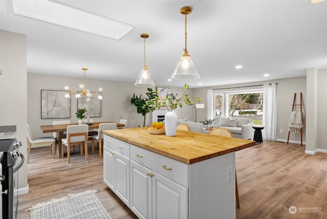 kitchen featuring pendant lighting, butcher block countertops, stainless steel electric range, white cabinetry, and a center island