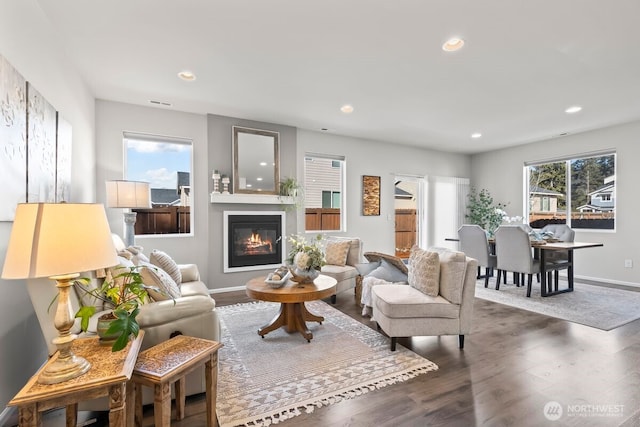 living room with dark wood-type flooring, a glass covered fireplace, a wealth of natural light, and recessed lighting