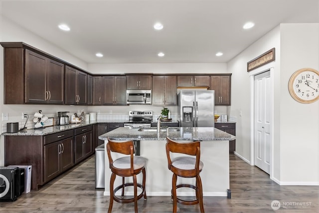 kitchen featuring a kitchen island with sink, appliances with stainless steel finishes, a sink, and dark brown cabinetry