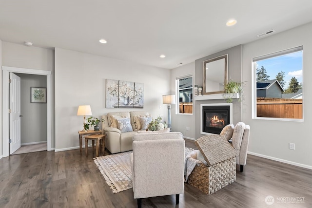 living area featuring recessed lighting, dark wood finished floors, baseboards, visible vents, and a glass covered fireplace