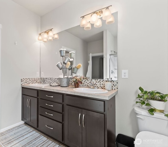 full bath featuring double vanity, a sink, toilet, and decorative backsplash