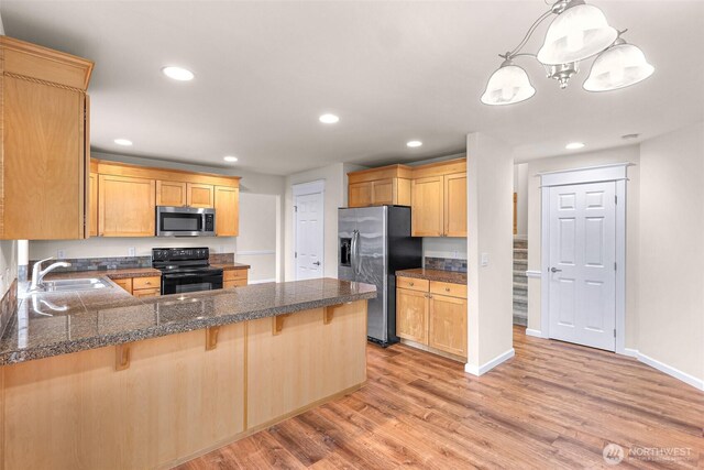 kitchen with light wood finished floors, stainless steel appliances, hanging light fixtures, a sink, and a peninsula