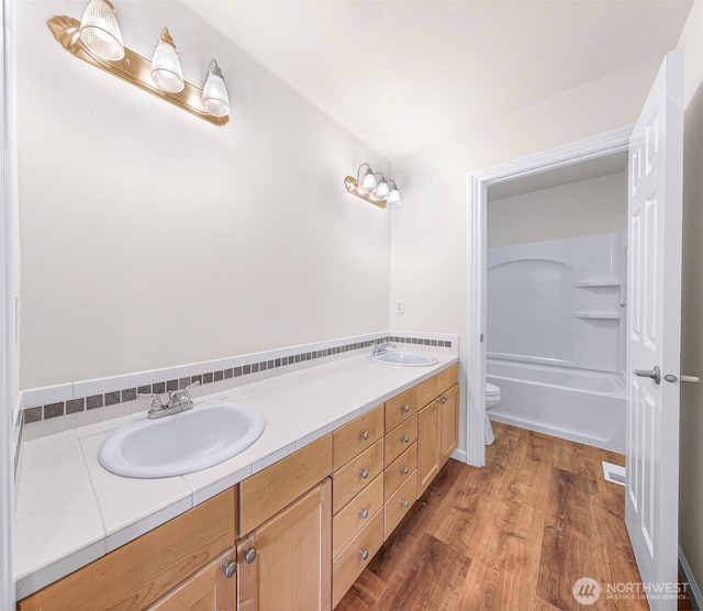 full bathroom featuring toilet, double vanity, a sink, and wood finished floors