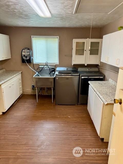 kitchen with sink, light hardwood / wood-style flooring, washing machine and dryer, and white cabinets