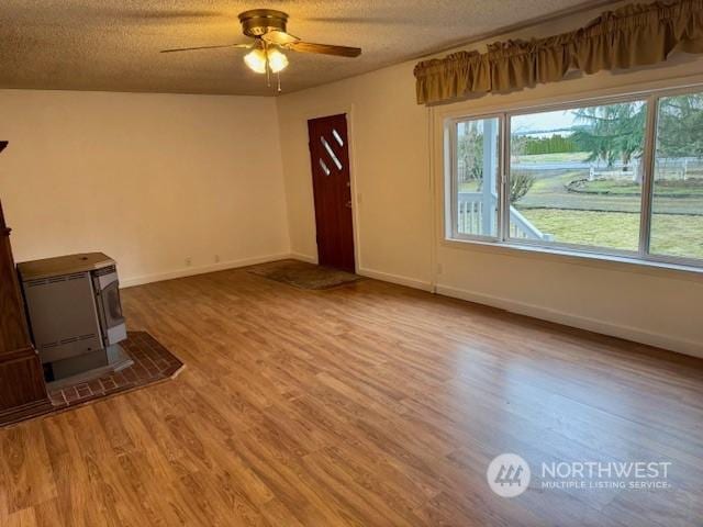 unfurnished living room with hardwood / wood-style floors, ceiling fan, a textured ceiling, and a wood stove