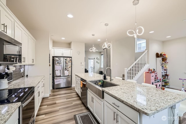 kitchen with decorative light fixtures, an island with sink, white cabinetry, sink, and stainless steel appliances