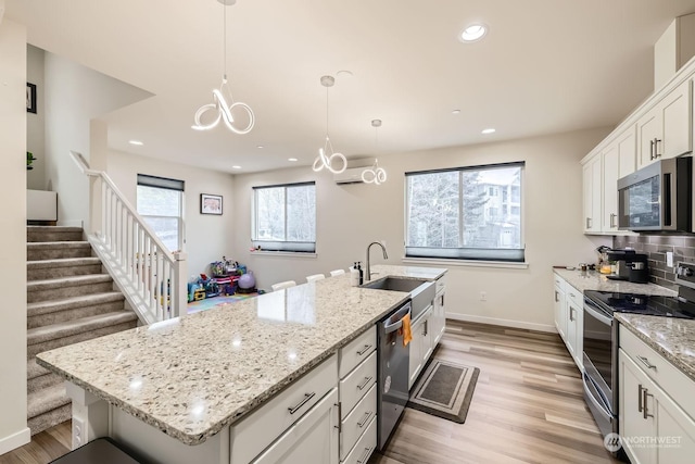 kitchen featuring white cabinetry, appliances with stainless steel finishes, a kitchen island with sink, and pendant lighting