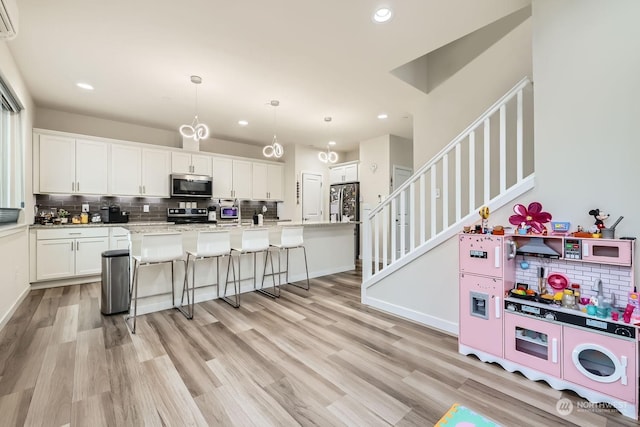 kitchen featuring hanging light fixtures, white cabinetry, appliances with stainless steel finishes, and a kitchen breakfast bar