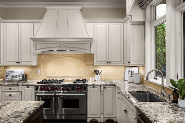 kitchen featuring a sink, range with two ovens, custom exhaust hood, and white cabinetry