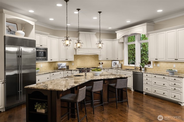 kitchen with a kitchen island with sink, open shelves, crown molding, and built in appliances