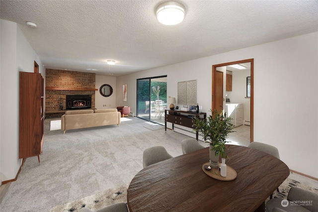 dining room featuring a brick fireplace, light carpet, washing machine and clothes dryer, and a textured ceiling