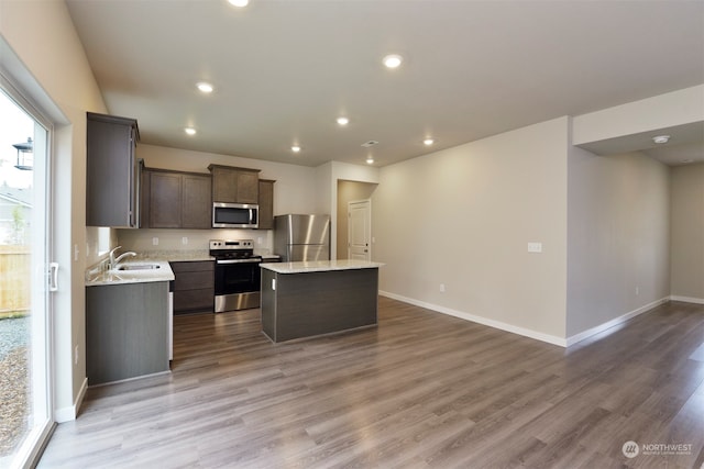 kitchen with sink, light stone counters, wood-type flooring, a center island, and appliances with stainless steel finishes