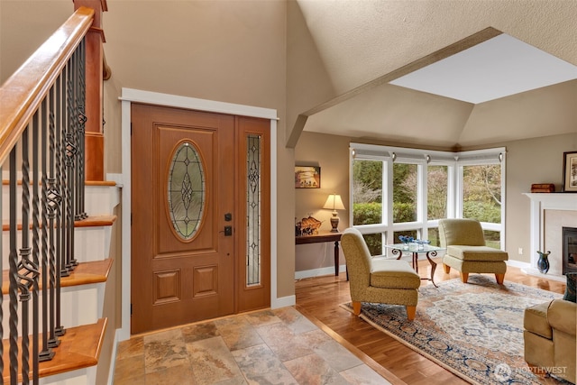 entryway with stairway, baseboards, lofted ceiling, light wood-style floors, and a tiled fireplace