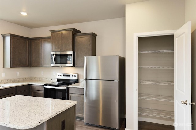 kitchen featuring stainless steel appliances, a kitchen island, light stone countertops, and dark brown cabinetry