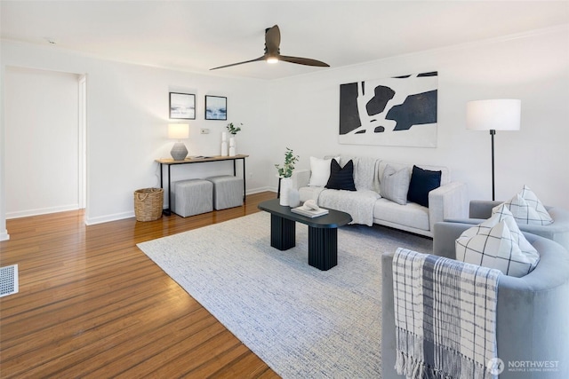 living room featuring a ceiling fan, visible vents, baseboards, and wood finished floors