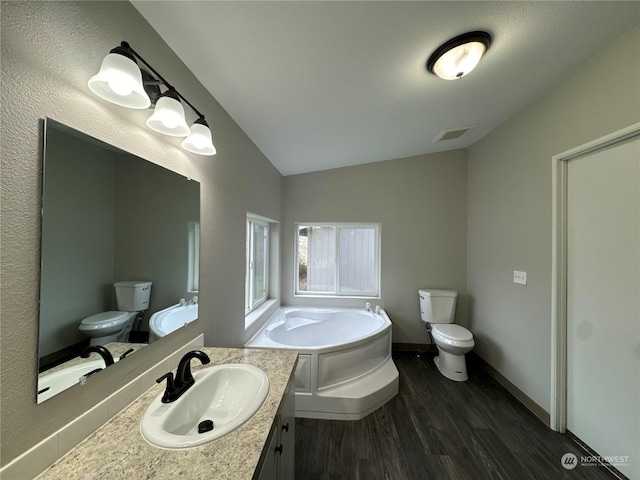 bathroom with vaulted ceiling, wood-type flooring, a tub to relax in, vanity, and toilet