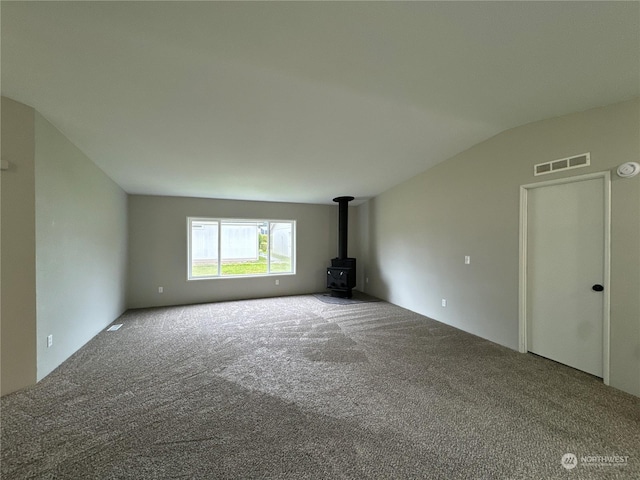 unfurnished living room featuring lofted ceiling, carpet floors, and a wood stove