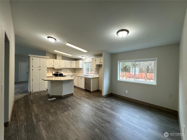 kitchen with vaulted ceiling, a kitchen island, dark hardwood / wood-style floors, appliances with stainless steel finishes, and white cabinetry