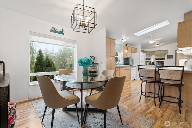 dining space featuring light hardwood / wood-style flooring, vaulted ceiling with skylight, and a chandelier