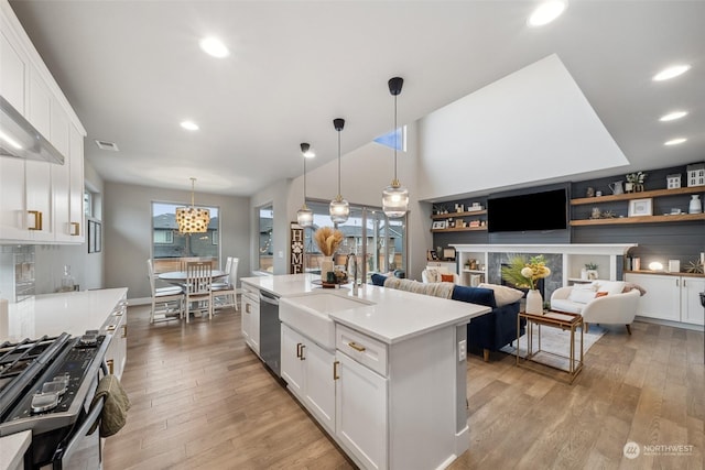 kitchen with sink, appliances with stainless steel finishes, an island with sink, white cabinets, and decorative light fixtures