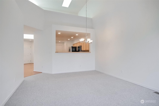 unfurnished living room featuring an inviting chandelier, light colored carpet, and a high ceiling