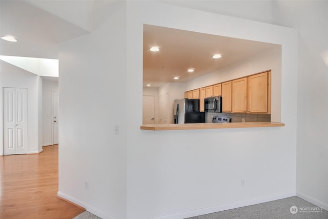 kitchen with appliances with stainless steel finishes, light brown cabinetry, decorative backsplash, light hardwood / wood-style floors, and kitchen peninsula