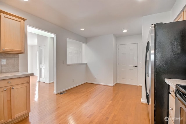 kitchen featuring tile countertops, light brown cabinets, stainless steel appliances, light hardwood / wood-style floors, and backsplash