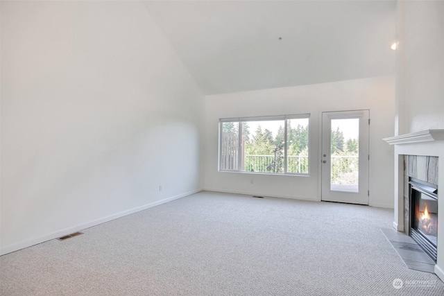 unfurnished living room with a tiled fireplace, high vaulted ceiling, and light colored carpet