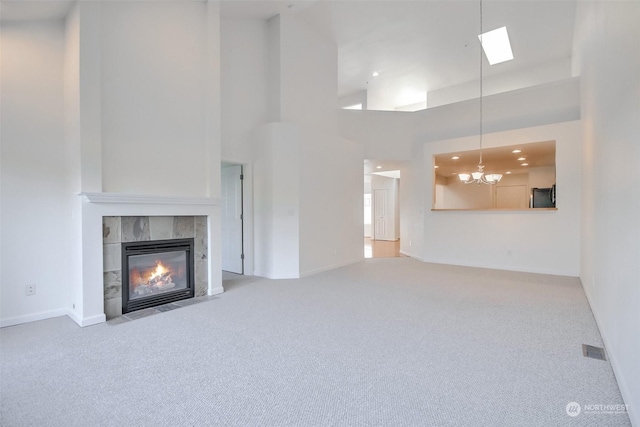 unfurnished living room with an inviting chandelier, carpet floors, a tile fireplace, and a high ceiling