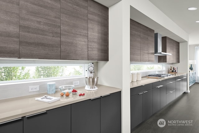 kitchen featuring wall chimney range hood, dark wood-type flooring, a wealth of natural light, and stainless steel gas cooktop