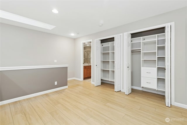 unfurnished bedroom featuring multiple closets, a skylight, and light hardwood / wood-style flooring