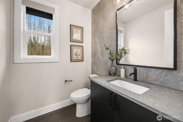 half bath with toilet, wood finished floors, vanity, baseboards, and tasteful backsplash